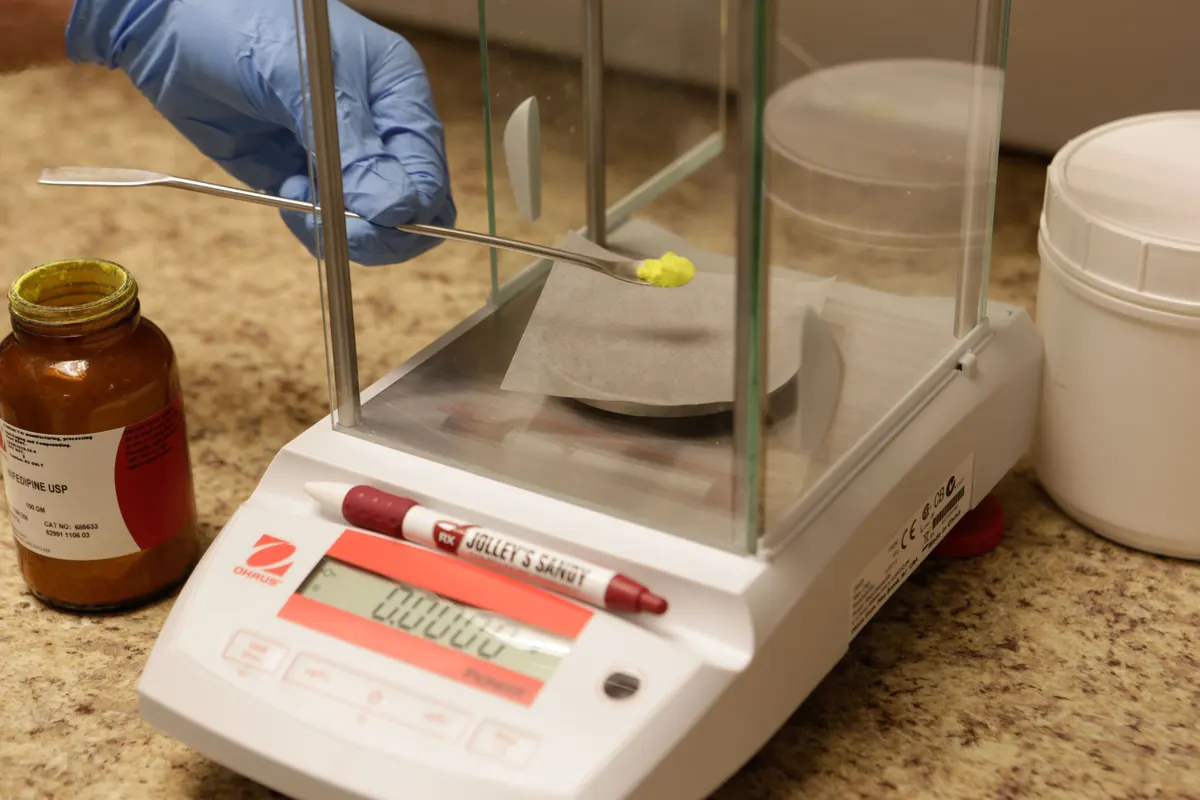 A pharmacy team member precisely weighing an ingredient for a compounded medication