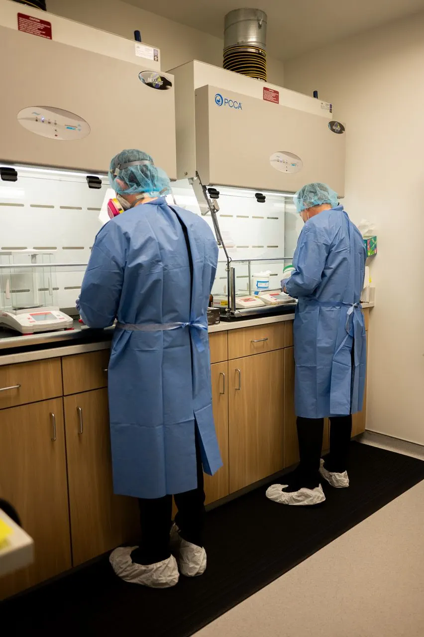 Two pharmacy team members preparing medications inside the compounding lab