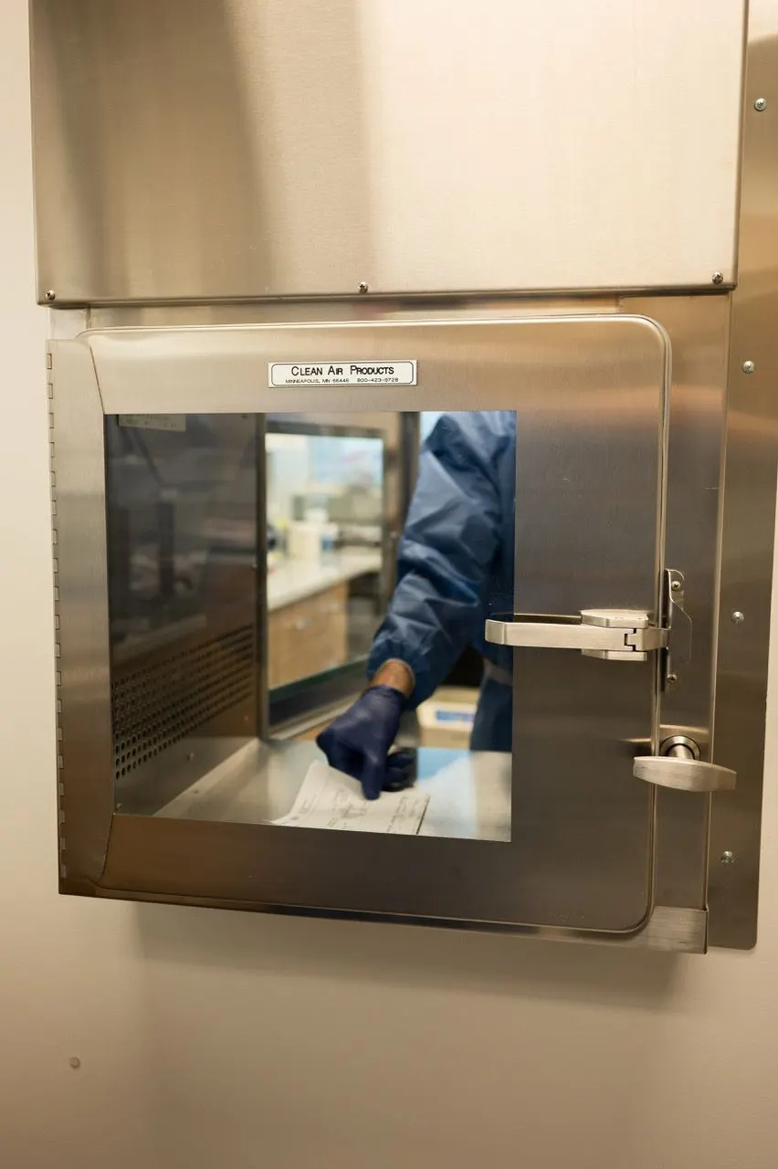 A gloved pharmacy team member working through a clean-air compounding enclosure